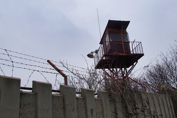 A concrete fence with a metal fence and an observation tower for armed guards to a prison or...