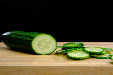 Sliced ​​cucumber on a wooden board on a black background
