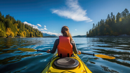 Person kayaking in a vibrant mountain lake surrounded by lush forests and majestic peaks on a sunny day.