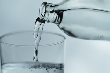 Water from bottle pouring into glass on table, isolated on white background. clean water for a good health. Mineral water in glass. Image of clean water from nature.