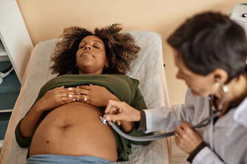 Top down view of pregnant African American woman lying on clinic bed with closed eyes while...