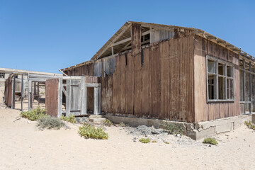 forsaken corrugated-iron building on sand at mining ghost town in desert, Kolmanskop,  Namibia