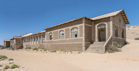 Fototapeta na wymiar forsaken hospital buildings on sand at mining ghost town in desert, Kolmanskop, Namibia