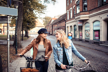 Two happy women cycling together on city street