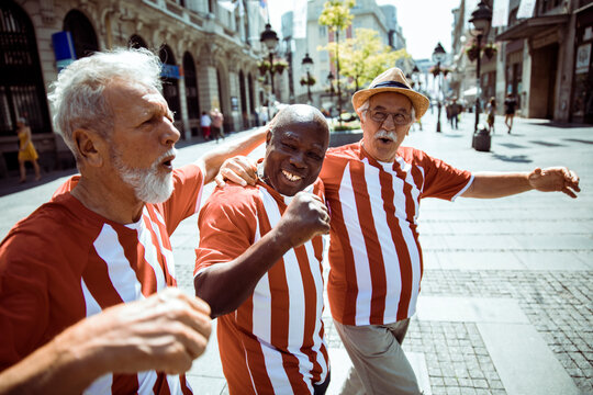 Senior friends celebrating and singing in matching striped shirts on city street