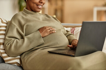 Cropped shot of smiling pregnant Black woman working on laptop while putting hand on her big belly...