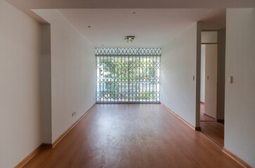 Apartment living room with wood-colored laminate floor, partition with grille and view to the street.