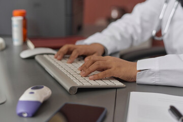 Hands of unrecognizable female doctor typing on computer keyboard sitting at desk at her workplace