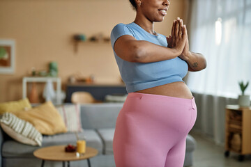Cropped shot of Black expectant mother in crop top and leggings working out at home while putting hands in yoga prayer pose