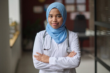 Female doctor in hijab standing at clinic with her arms crossed and confidently smiling at camera