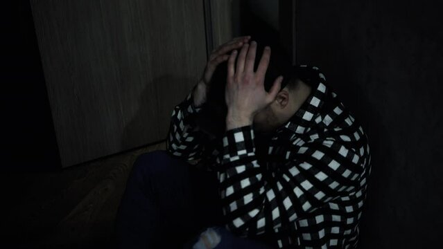 People's life problems, A man in a dark room sitting in the corner of the room, an upset man holding his head with his hands, a pensive man, social problems. Depression.