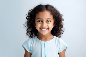 portrait of a happy smiling little girl with curly hair, Indian appearance, in a pale blue dress on a blue background. children's joy and happiness for parents.A child's smile