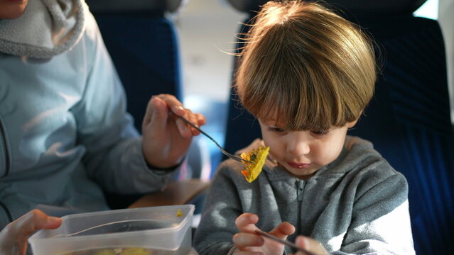 Mother feeding son during train trip. Child passenger being fed food while traveling. Mom holding tupperwear and fork