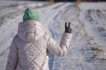 Kobieta pokazuje gest Victorii. Symbol „V” widoczny z tyłu. Słoneczna pogoda w czasie zimy.