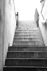 Betonowe schody prowadzące ludzi pod podziemne przejście. Szaro-białe zdjęcie schodów prowadzących pod most. Poręcz przymocowana do ściany przy schodach wykonanych z betonu. - obrazy, fototapety, plakaty
