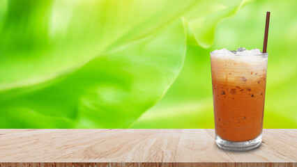 Iced thai milk tea in glass, Milk ice tea, Cheddar is a traditional Thai drink on wooden table with nature background, Summer drinks with iced