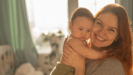A Caucasian woman tenderly holds her newborn son in the morning rays of sunlight.