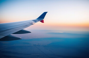 Fototapeta premium Aircraft wing. Beautiful sunset, sky. Top view. Airplane flying view from window. Traveling. Passenger plane is above clouds during sundown. Sunrise flight. Commercial jet. Aerial view from a porthole