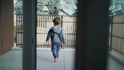 Small boy opening door to apartment's balcony. Child going to home terrace leaning on barrier