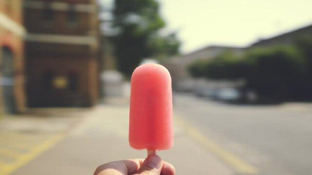 Spinning, popsicle or hand of person in city eating strawberry flavor dessert for travel pov in street. Outdoor, urban or closeup of a yummy frozen snack or sweet treat on pavement or road in motion