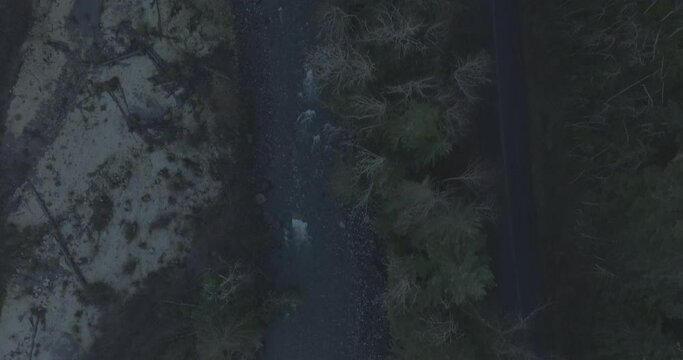 Ungraded 4k high-angle aerial drone footage of a rural mountain road alongside a river on a dark winter morning in Washington State.