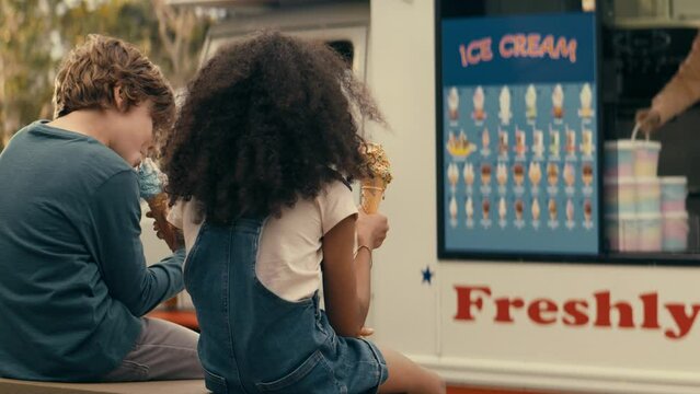 Little boy and little girl eating ice cream while looking at the ice cream truck