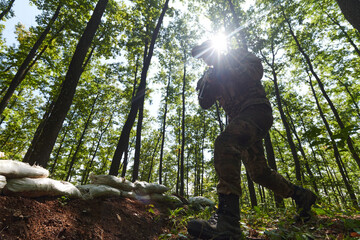 An elite soldier adeptly clears military barriers in the perilous wooded terrain, showcasing...