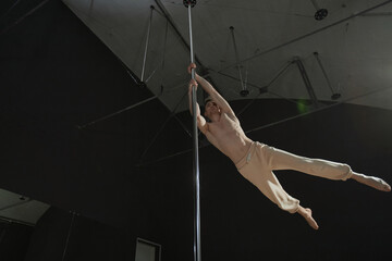 Low angle view of fit Caucasian bare to waist male pole dancer spinning on pylon preparing for trick