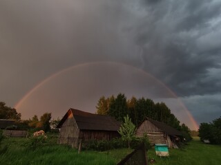 rainbow over rural barns in the village, against the backdrop of dark blue clouds in rainy weather