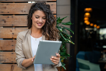 Young business woman manager wearing suit using digital tablet for work outside modern Cafe.