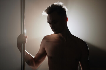 Backlight shot of unrecognizable muscular male exotic dancer holding on to pole standing in dimly...