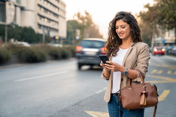 Cheerful business woman smiling at her smartphone while commuting to the office in the city. Young...
