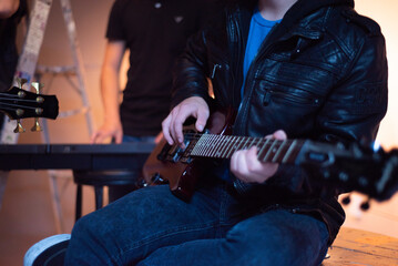 Musica. Güitarrista con chaqueta de cuero, sentado, con su Güitarra, en un ensayo de banda.