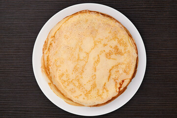 A round dish with fried pancakes on a brown table. Sweet dessert. Top view.
