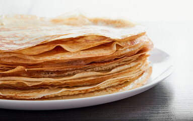A round dish with fried pancakes on a brown table. A sweet dessert for breakfast. Sunny morning.