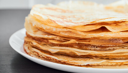 A round dish with fried pancakes on a brown table. A sweet dessert for breakfast. Sunny morning.