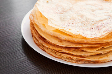 A round dish with fried pancakes on a brown table. A sweet dessert for breakfast. Sunny morning.