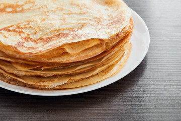 A round dish with fried pancakes on a brown table. A sweet dessert for breakfast. Sunny morning.