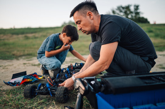 Father and his son fixing toy cars after fun racing time, outdoors.