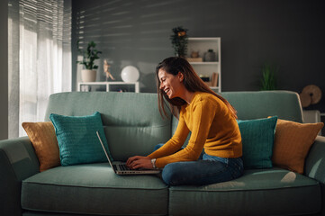 Smiling woman using laptop and checking email while sitting on the couch at home