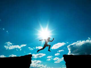 A man jumps over a gorge against a sky with clouds. Success concept.