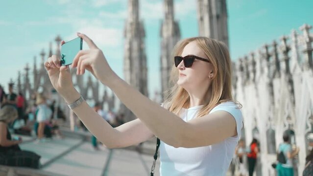 Selfie girl. Young female tourist making selfie photo with smart phone on the roof of the famous Duomo cathedral in Milan. Happy vacations in Milan