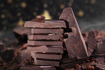 Broken dark chocolate bar and chocolate flakes on black kitchen table