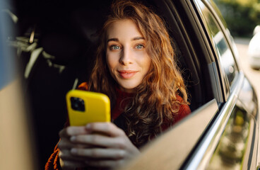 Young woman uses a smartphone while sitting in the back seat of a car. The concept of business,...