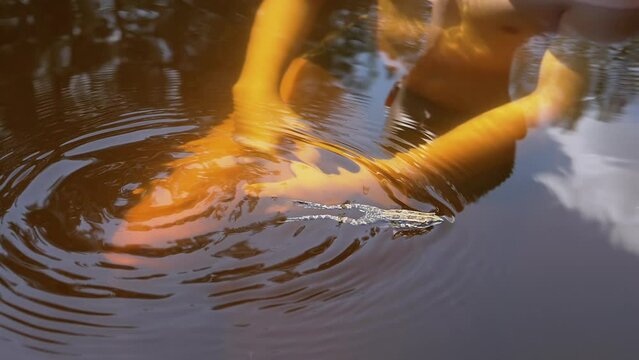 Close up, a Child Playing with a Frog Underwater while Swimming in a Pond. Spotted frog swims in a quiet river, reflected in water in bright sunlight. Sunny day, summer, outdoor recreation. Wildlife.