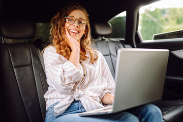 Young woman uses laptop in car. Remote work. Business, blogging, freelance, Online shopping, education concept.