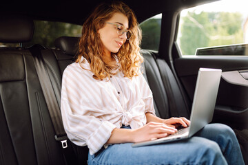 Young woman uses laptop in car. Remote work. Business, blogging, freelance, Online shopping, education concept.