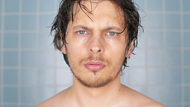 Man, morning and shower for hygiene, grooming or cleanliness in bathroom on wall background. Portrait of wet and serious male person or model with clean face for washing, cleaning or skincare at home
