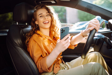 Beautiful woman driver in a car with a phone. Paying for parking and navigating in the city. Leisure, travel, technology, bussines.