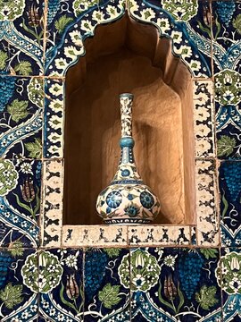 Close up of beautiful exotic tiles oriental moroccan style floral and pattern symmetry in blues white and gold on wall with high stem ceramic antique vase on shelf in alcove in Leighton House London